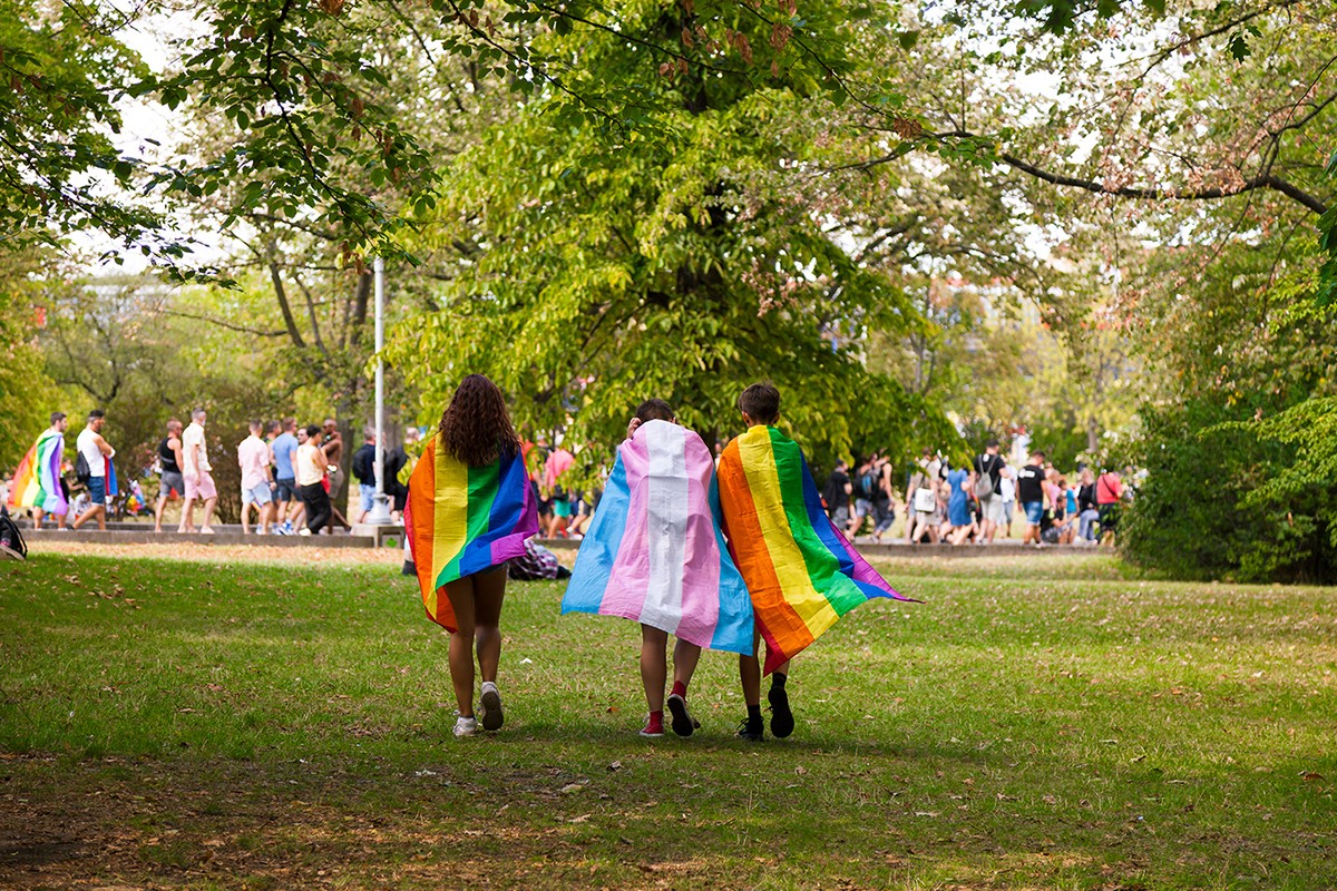 Tres persones amb banderes trans i LGTBIQ+ adreçant-se a una manifestació del col·lectiu